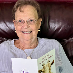 Elderly woman joyfully laughing while holding a humorous birthday card.